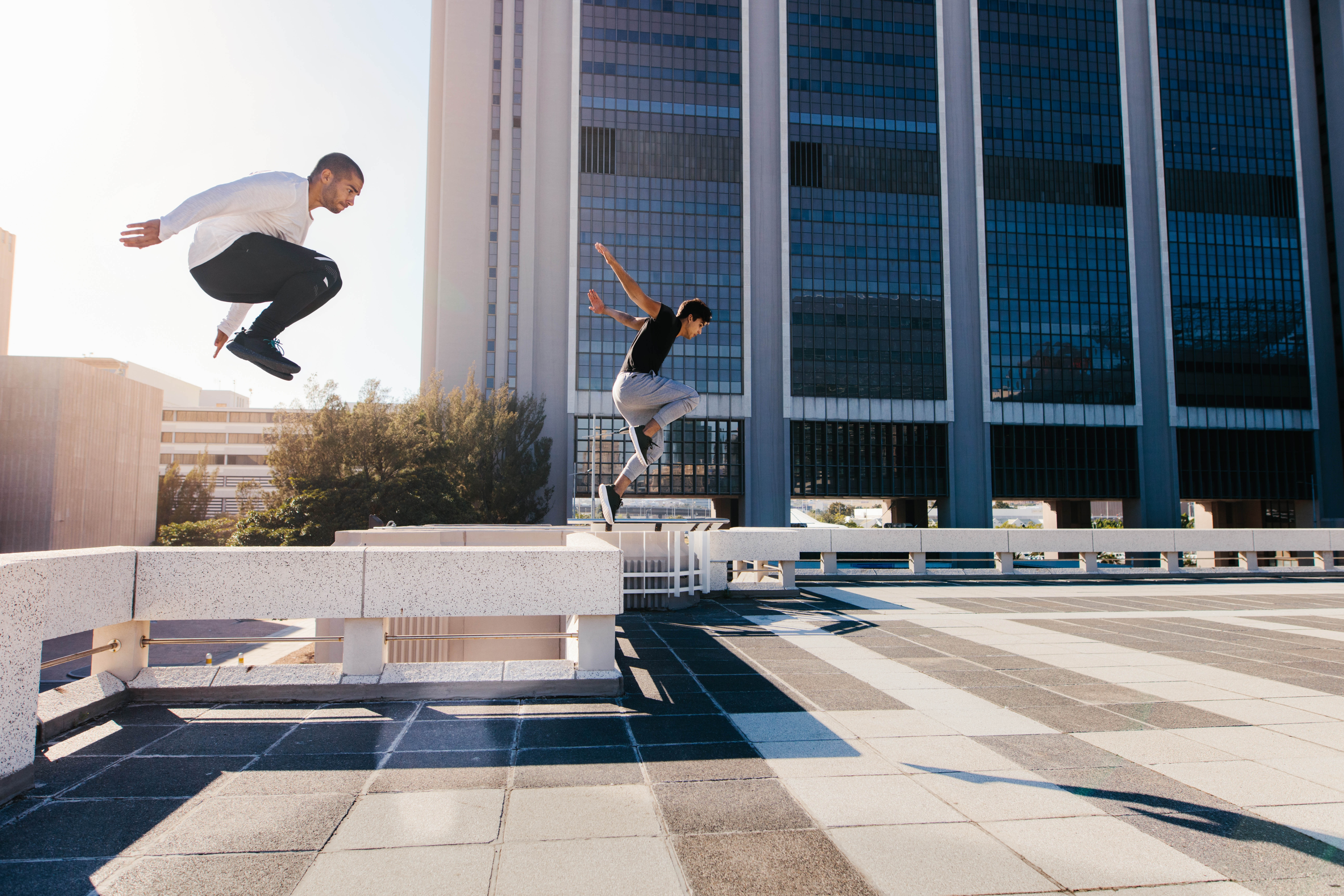 Two young Latino men jumping off of concrete barriers in a city